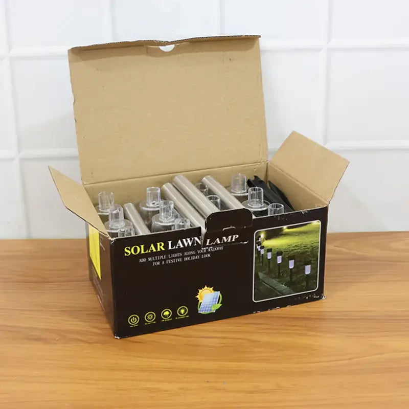 Open box of solar lawn lamps on a wooden surface with a white tiled wall background.