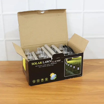 Open box of solar lawn lamps on a wooden surface with a white tiled wall background.