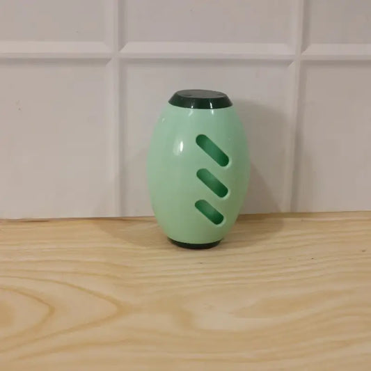 Green cylindrical object with black top and bottom on a wooden surface with tiled wall background