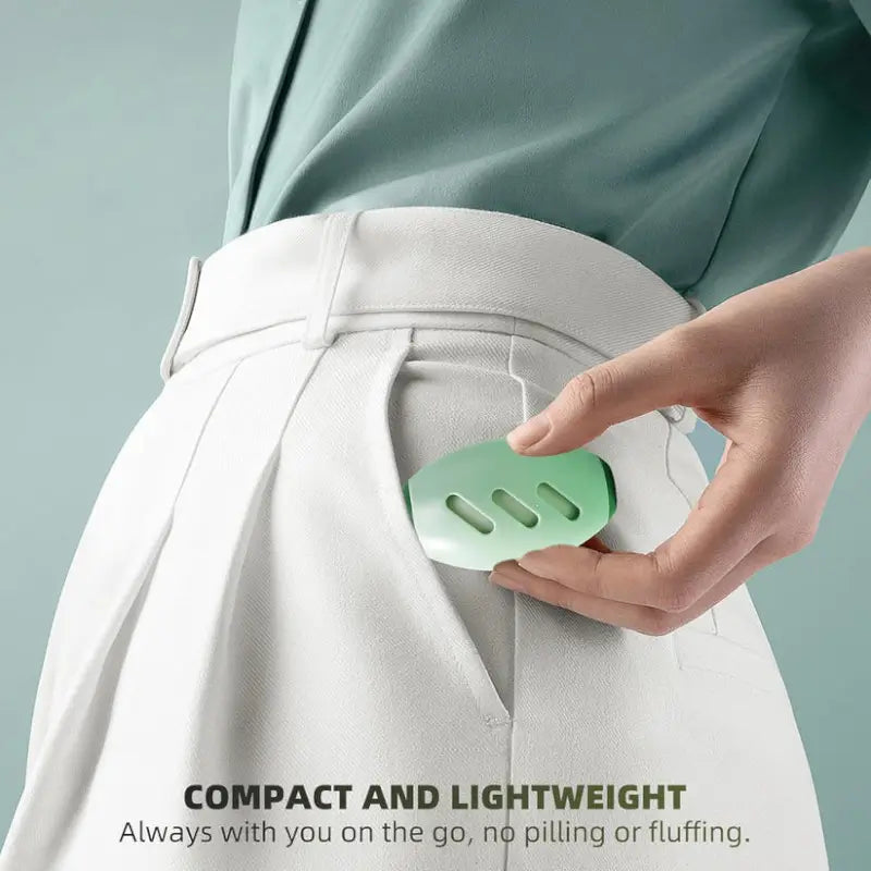 Hand holding a green fabric shaver against white pants with text 'Compact and Lightweight' on a light gray background.