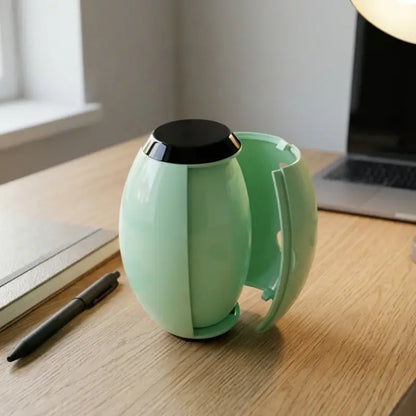 Green mug with black lid on a wooden desk next to a laptop and pen